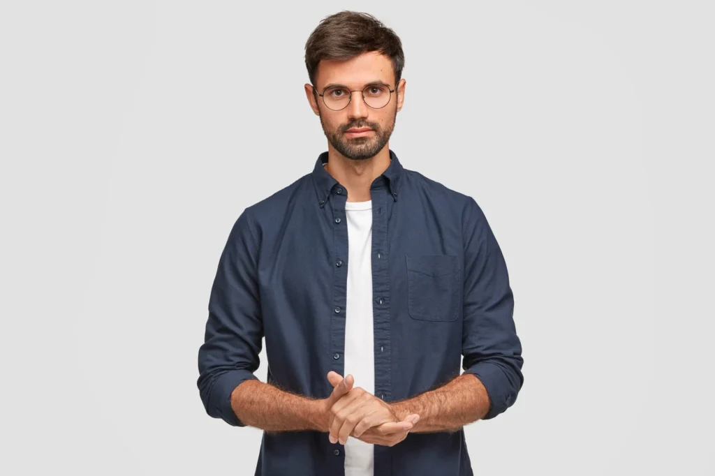 waist-up-portrait-handsome-serious-unshaven-male-keeps-hands-together-dressed-dark-blue